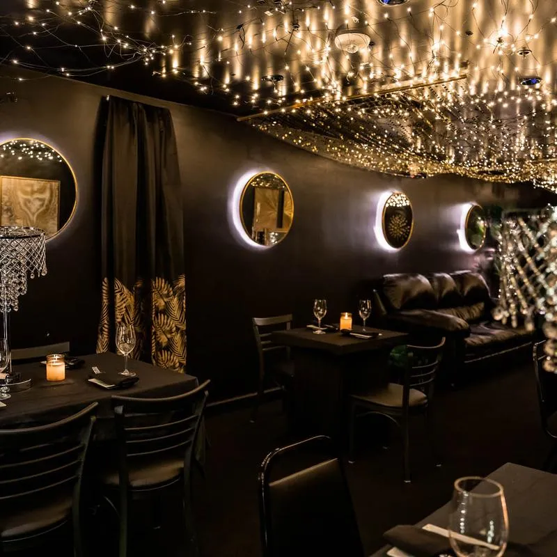 A black-and-gold lounge room at TK's Comedy with string lights and round mirrors