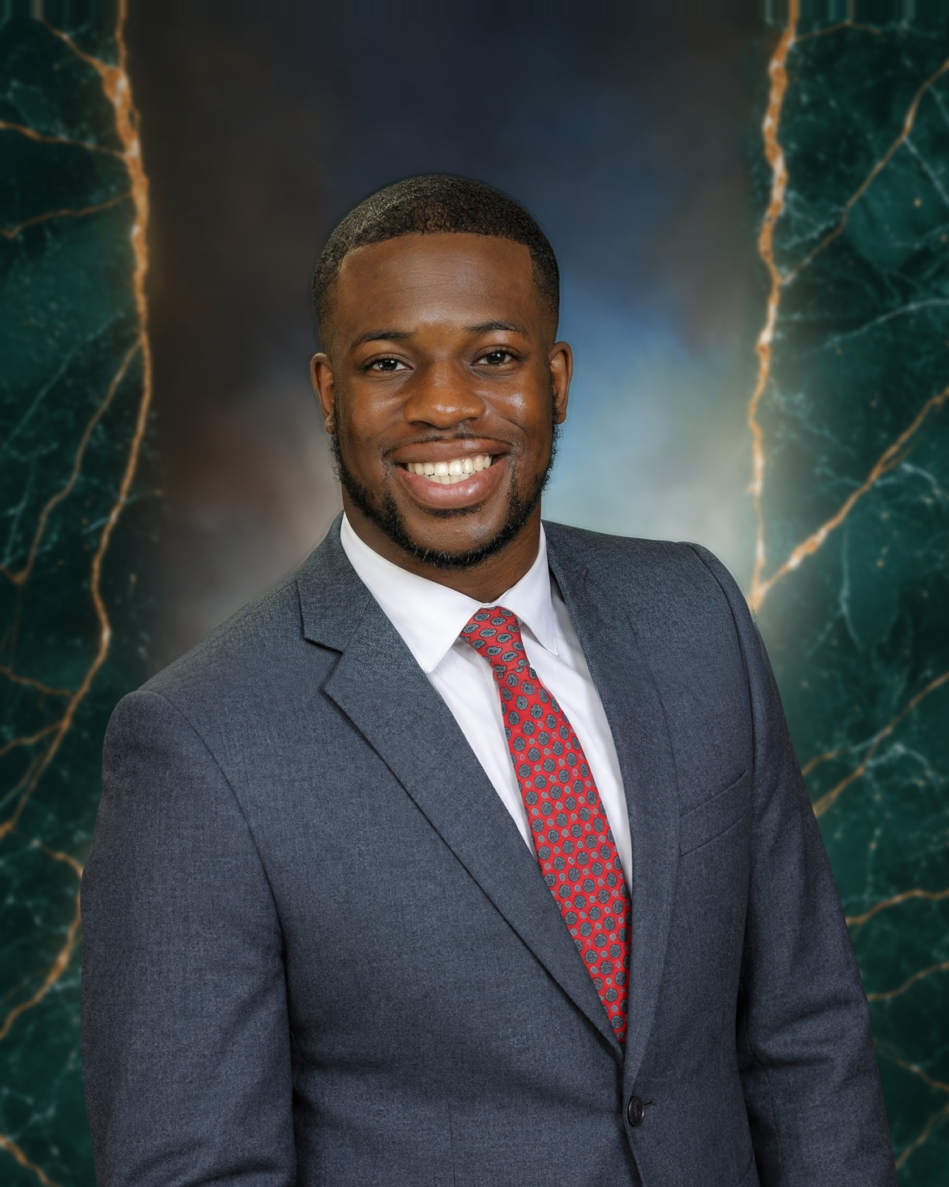 Dr. Randy Obi smiling in a gray suit, white shirt and red patterned tie against a green marble backdrop
